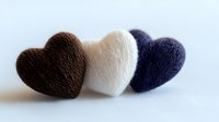 Three knitted heart shapes in brown, white, and navy blue arranged in a row on light fabric background, perfect for craft projects and Valentine's Day designs.