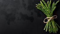 Fresh green asparagus bunch tied with twine string on dark background. Raw organic vegetables with copy space for menu, recipe or healthy eating concept.