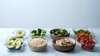 Healthy meal prep containers with fresh vegetables, avocado, nuts, oatmeal and berries arranged on white background for weekly planning and nutrition.