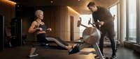 Personal trainer coaching blonde woman on rowing machine in modern luxury gym with warm lighting and wooden wall design for fitness motivation.