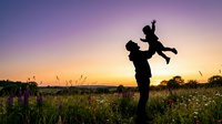 Father lifting child in air at sunset in wildflower meadow, celebrating parenthood and family bonding outdoors during golden hour.