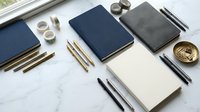 Professional workspace with elegant notebooks, pens and office supplies arranged on marble surface for business planning and creative writing projects.