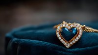 Heart-shaped sapphire pendant with diamond halo on gold chain resting on dark teal velvet jewelry box, macro jewelry photography with soft focus.