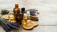 Essential oils in amber glass bottles with lavender sprigs, dried orange slices and cinnamon sticks on rustic wooden background for aromatherapy and wellness.