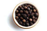Aromatic black peppercorns in white ceramic bowl on white background, overhead view of whole dried spice for cooking and seasoning food preparation.