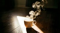 Steaming hot cup of coffee or tea on a wooden floor with dramatic light and rising smoke in a cozy dark atmosphere.