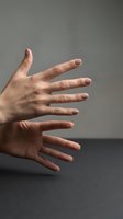 Two female hands with nude manicure stretched out against a gray background, fingers spread wide, minimalist beauty and wellness concept.