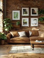 Modern living room interior with brown leather sofa against exposed brick wall, decorated with framed landscape photos and potted plants. Natural light streams across hardwood floor.