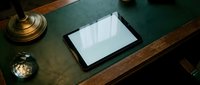 Digital tablet with blank white screen on wooden desk with vintage brass lamp and decorative items for modern workspace mockup and technology presentation.