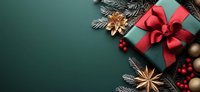 Green wrapped gift box with red satin bow, decorated with fir branches, star anise, red berries and golden ornaments on dark green background with copy space.