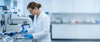 Female scientist in white lab coat working with microscope in modern research laboratory conducting medical analysis and scientific experiments.