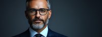 Confident mature businessman with gray hair and beard wearing glasses and navy suit against dark background, professional corporate portrait in panoramic format.