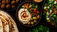 Middle Eastern mezze spread with hummus, falafel, fresh salad, olives, and warm pita bread on dark wooden table, traditional Mediterranean appetizers served family style.