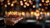 Glowing candles in glass holder with golden bokeh lights background, hand holding romantic candlelight creating cozy festive atmosphere for celebration.