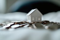 Small white model house placed on pile of silver coins against blurred background, representing real estate investment and property finance concept.