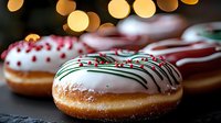 Festive holiday donuts with white icing, green drizzle, and red sprinkles against blurred golden bokeh lights for seasonal celebrations.