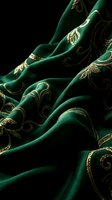 Luxurious emerald green fabric with ornate golden embroidered swirls and decorative patterns draped elegantly against dark background for premium textile design.