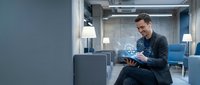 Young Caucasian businessman smiling while using tablet with glowing legal hologram interface in modern blue-toned office lounge.