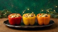 Three colorful stuffed bell peppers with herbs on dark plate, festive holiday dinner preparation with Christmas decorations and warm lighting background.