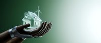 Hands holding glowing eco-friendly house model with wind turbine representing sustainable energy and green building technology for environmental conservation.