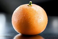Fresh ripe orange with water droplets on dark surface. Healthy citrus fruit for nutrition, diet, vitamin C concepts and culinary photography.
