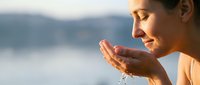 Young woman cupping fresh water in hands by serene lake at sunset, peaceful moment of connection with nature for wellness and mindfulness content.