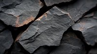 Dark layered slate rock fragments with rough textured surface and natural cracks showing earthy tones and geological patterns in dramatic lighting.