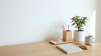Minimalist wooden desk workspace with notebook, plant, mug and reed diffuser on clean white background for home office and productivity concepts.
