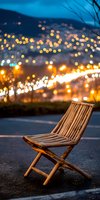 Empty bamboo folding chair against evening cityscape with blurred bokeh lights creating magical atmosphere. Peaceful urban nighttime scene for relaxation concepts.