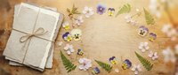Vintage letters tied with twine surrounded by pressed wildflowers and fern leaves on rustic wooden background with copy space.