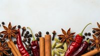 Aromatic spices and herbs arranged on white background including star anise, cinnamon sticks, dried chili peppers, cardamom pods and peppercorns for cooking.