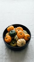 Assorted mini pumpkins and gourds in black bowl on white wooden surface for autumn harvest decoration and seasonal home styling.