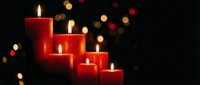 Red candles burning with warm flames creating cozy atmosphere against dark background with golden bokeh lights for holiday celebrations and romantic settings.