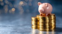 Pink ceramic piggy bank sitting on stacked gold coins against blurred bokeh background, symbolizing savings, financial growth and investment planning.