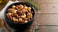 Mixed nuts and seeds in black bowl on rustic wooden table with rosemary herbs. Healthy snacking, cooking ingredients for recipes and meal preparation.