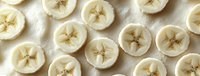 Fresh sliced bananas arranged in neat rows showing cross-sections with star pattern centers on white background, food photography for healthy eating concept.