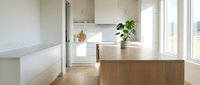 Modern kitchen with white cabinetry, wooden island, and natural light from large windows. Minimalist Scandinavian design with potted plant and warm wood flooring for contemporary home interiors.