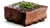 Juicy square cut beef steak cooked medium rare, garnished with fresh chopped herbs and coarse salt on dark background, close up view of meat texture.