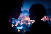 Romantic silhouettes of couple against blurred city lights at dusk, intimate moment with bokeh effect creating dreamy atmosphere in blue tones.