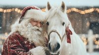 Festive winter scene with elderly bearded man in red velvet coat and hat embracing white horse against snowy backdrop with bokeh lights.