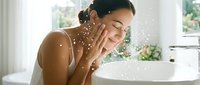 Young woman with medium skin tone splashing water on her face at bathroom sink, skincare and morning routine concept for wellness and beauty advertising.