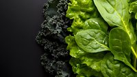 Fresh organic leafy greens including kale, lettuce and spinach arranged on dark background for healthy eating and nutrition concepts.