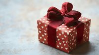 Red gift box with white hearts pattern and burgundy ribbon bow for Valentine's Day celebration and romantic occasions.
