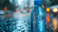 Cold plastic bottle with water drops on blue background with bokeh lights and reflections. Fresh drink concept for advertising and product photography.