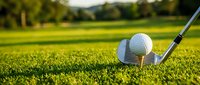 Golf ball on wooden tee with iron club on green course fairway during golden hour sunlight for sports and recreation activities.