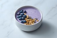 Purple smoothie bowl with fresh blueberries, granola and chia seeds on marble background. Healthy breakfast concept for clean eating and wellness lifestyle.