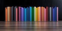 Row of colorful book spines arranged in rainbow spectrum order standing on reflective surface against dark background, creating mirror effect and modern minimalist composition.