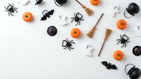 Halloween decorations with spiders, pumpkins, ghosts, bats and witch accessories scattered on white background for seasonal party planning and festive design.