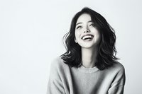 Young Asian woman with natural wavy black hair wearing light sweater laughing genuinely against white background, black and white portrait showing authentic joy and confidence.