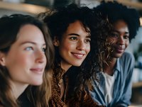 Three diverse young women smiling and laughing together in casual indoor setting, showing friendship, happiness and positive social connection.